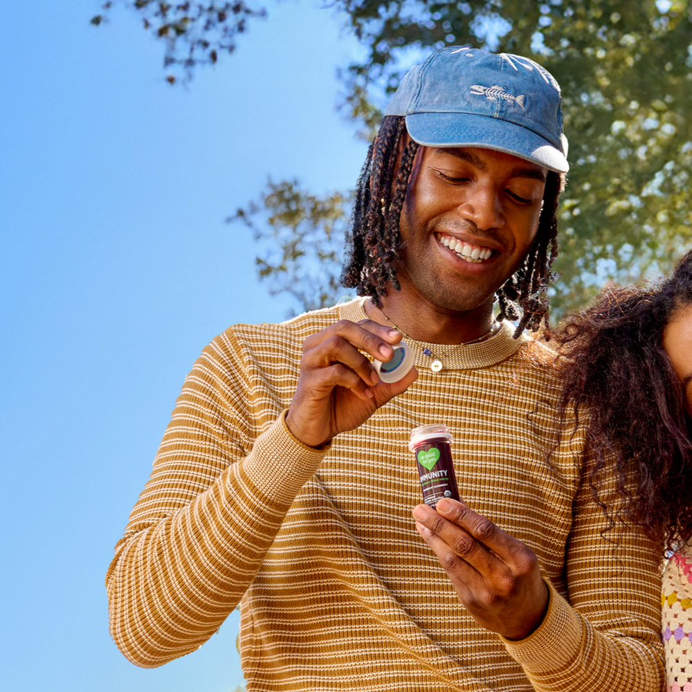 Two people standing outside underneath the trees holding So Good So You juice shots