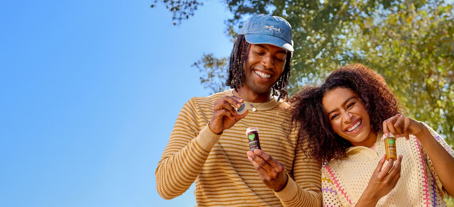 Two people standing outside underneath the trees holding So Good So You juice shots